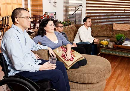 Man in a wheelchair watching television with family. (stock image)