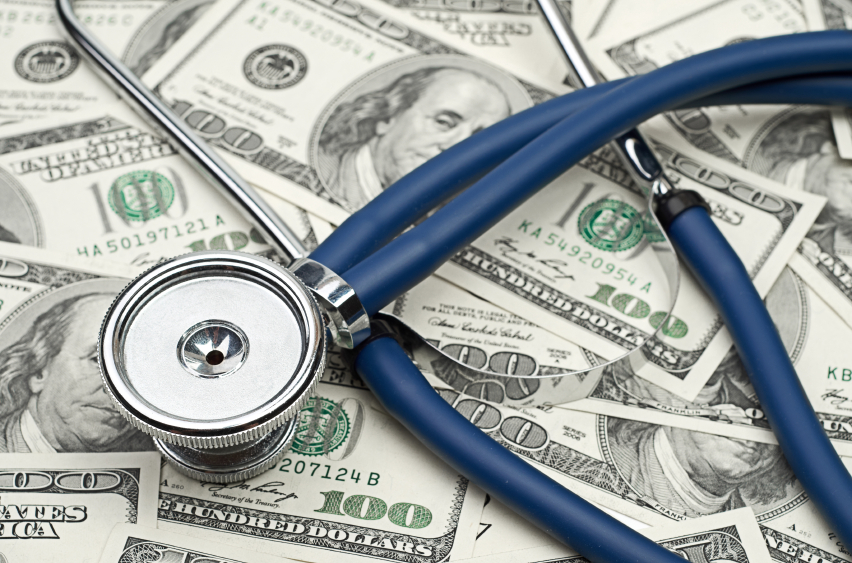 A stethoscope sits atop a pile of hundred dollar bills. (stock image)