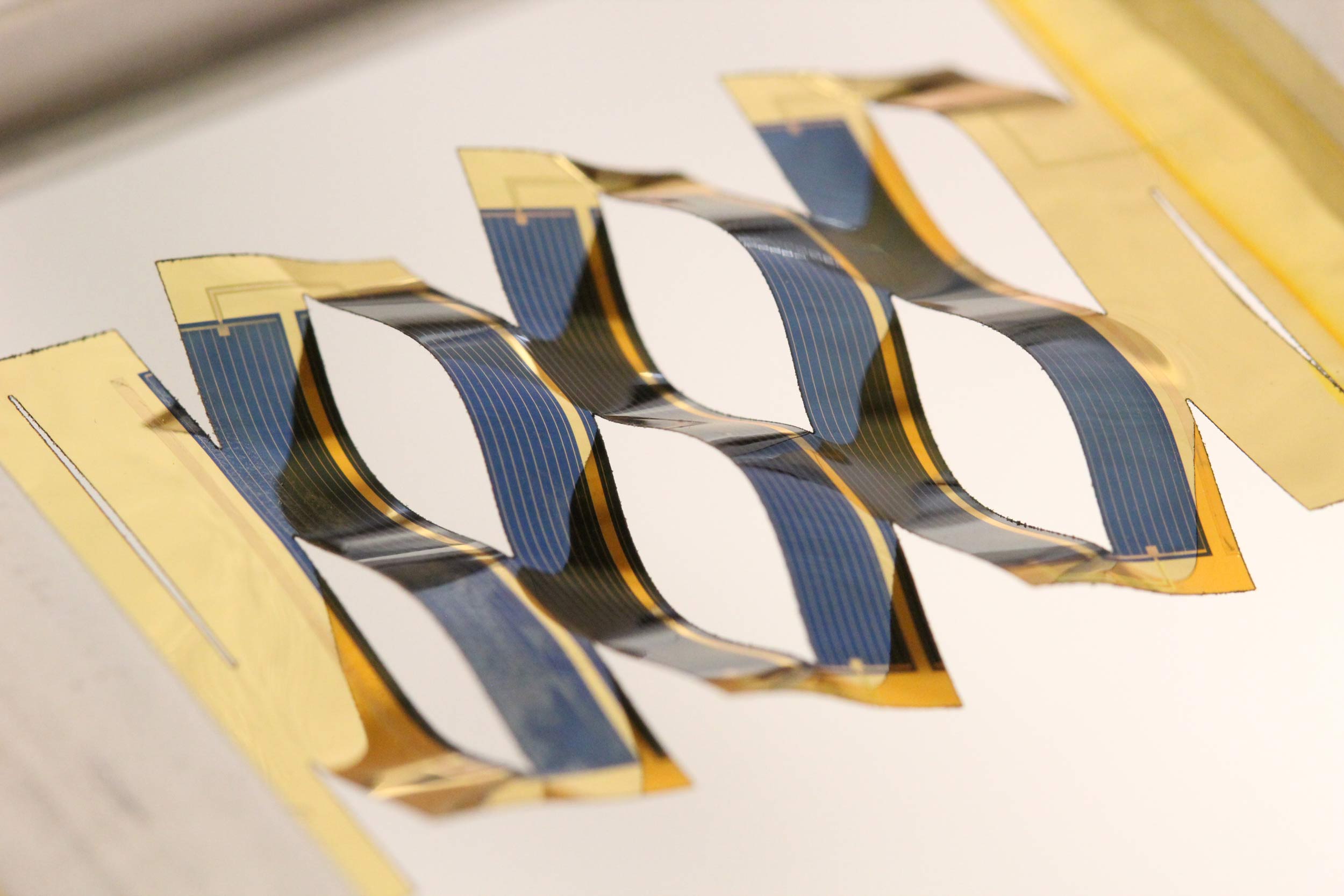 By borrowing from kirigami, the ancient Japanese art of paper cutting, researchers at the University of Michigan have developed solar cells that can track the sun. A flat plastic sheet backing the solar cells splits into wavy, connected ribbons when stretched. The tilt of the cells depends on the stretching, a simple mechanism for tracking the sun across the sky. Image credit: Aaron Lamoureux