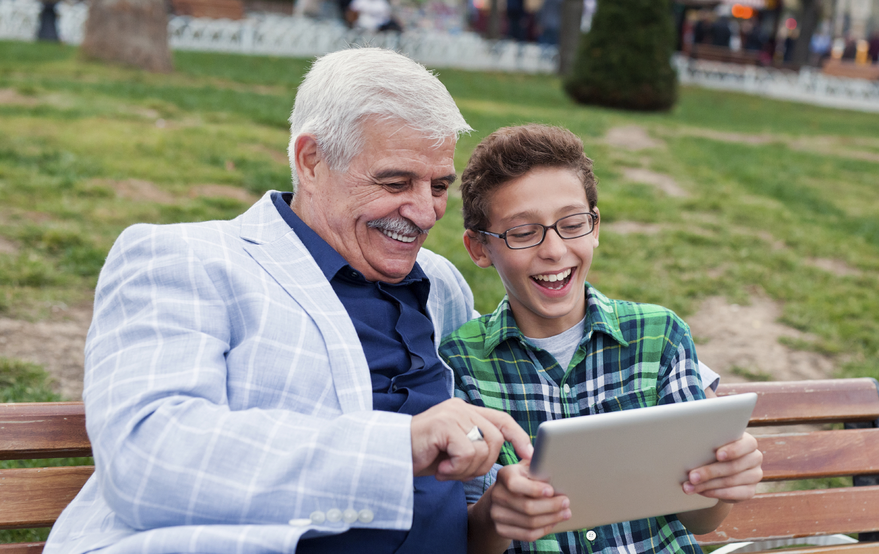 A senior man uses a tablet computer with a young teen. (stock image)