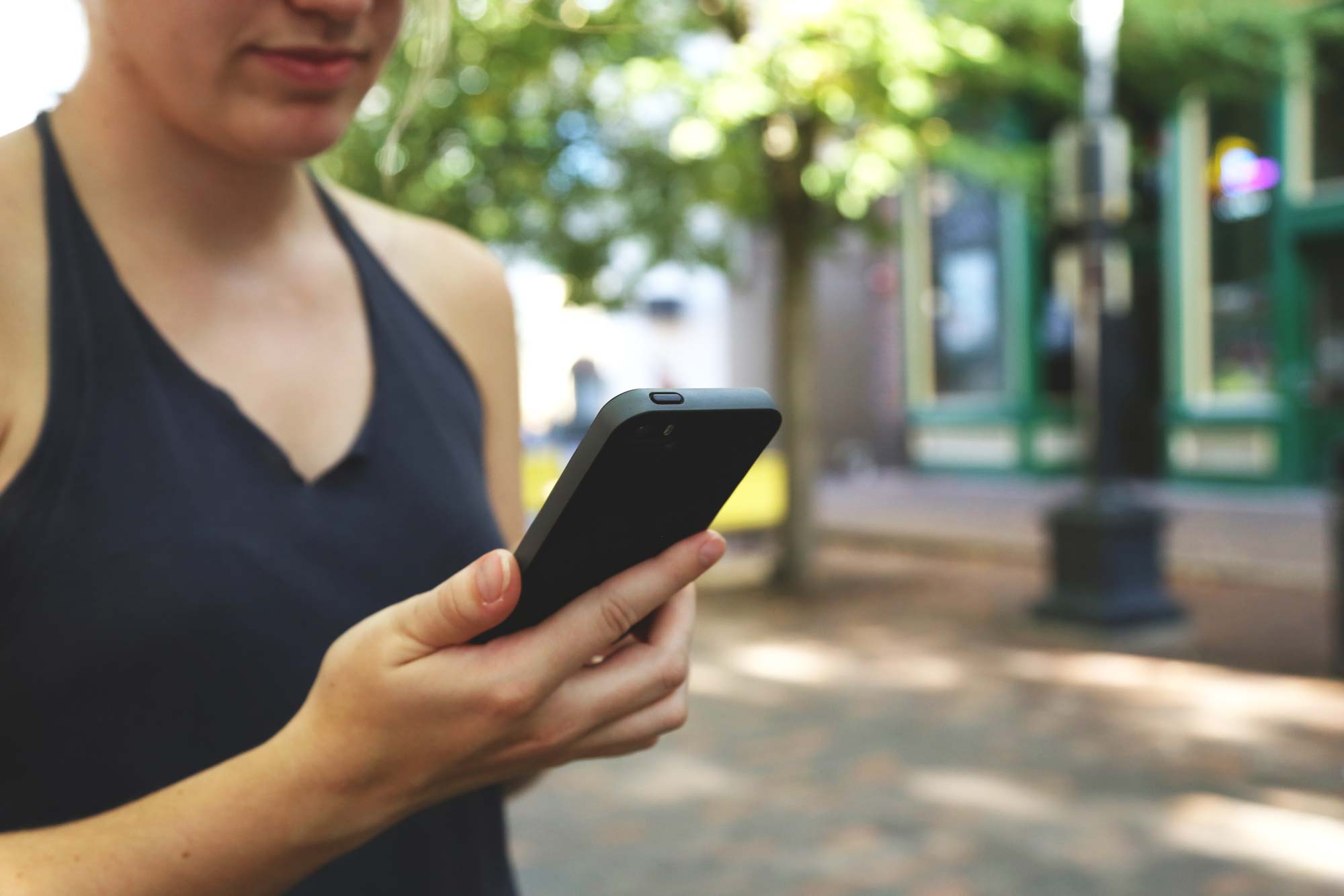 Cropped photo of a young woman looking at a cell phone. (stock image via Pexels)