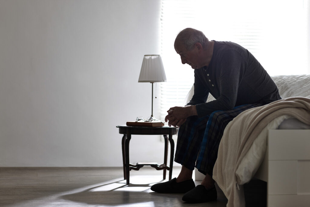 iStock image of an elderly man sitting on a bed. 