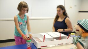 A girl places coins in her "bank" during the "trust" experiment involving a puppet. Image credit: Sean Moore, Michigan News