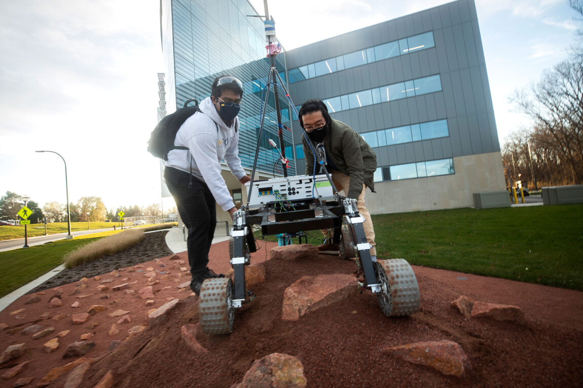 Photo of members of the Michigan Mars Rover team testing its rover on the Mars Yard outside of the Ford Robotics Building.