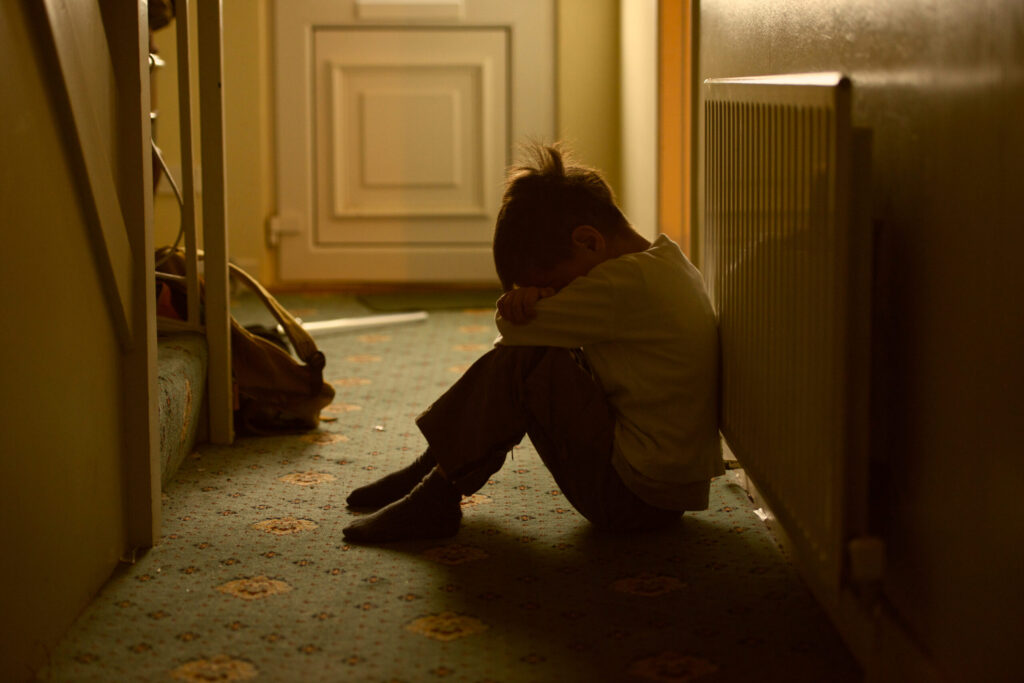 sad child with his head between his legs left alone at home. image credit: iStock