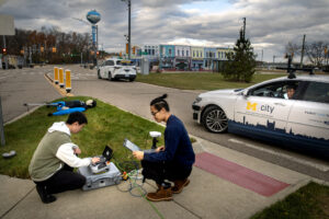 UM researchers Tinghan Wang (center) and Linxuan He (left) work on technology issues while Xintao Yan looks on from the challenge vehicle at Mcity on Friday afternoon, November 10, 2023. Tinghan Wang is the U-M researcher running the testing and a postdoc research fellow in Mechanical Engineering. The May Mobility shuttle is the back. Image credit: Marcin Szczepanski/Lead Multimedia Storyteller, Michigan Engineering