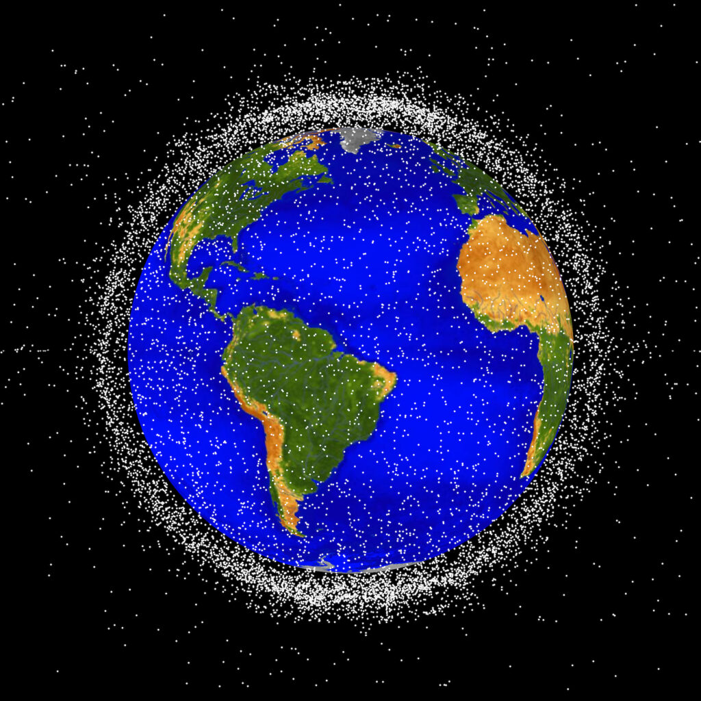 The space junk appears as many small white points surrounding Earth, which has bright blue oceans and green and brown continents.  The space junk is thick enough to form a cloud that obscures most of the black background when viewed from the edges around Earth.
