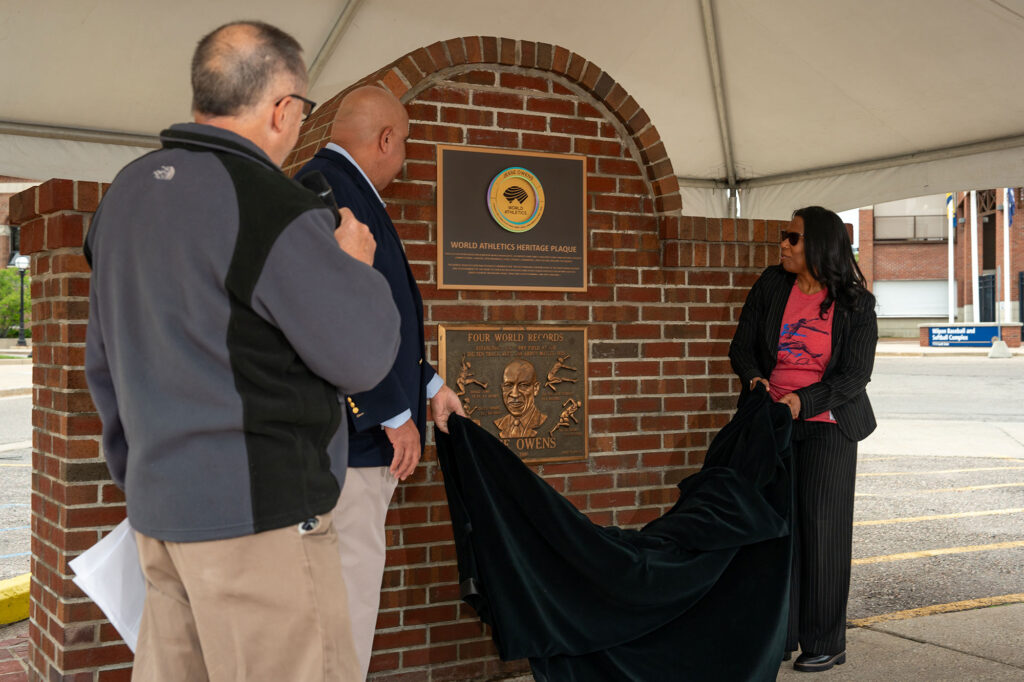 Photo of a man and woman unveiling a plaque as another man looks on.