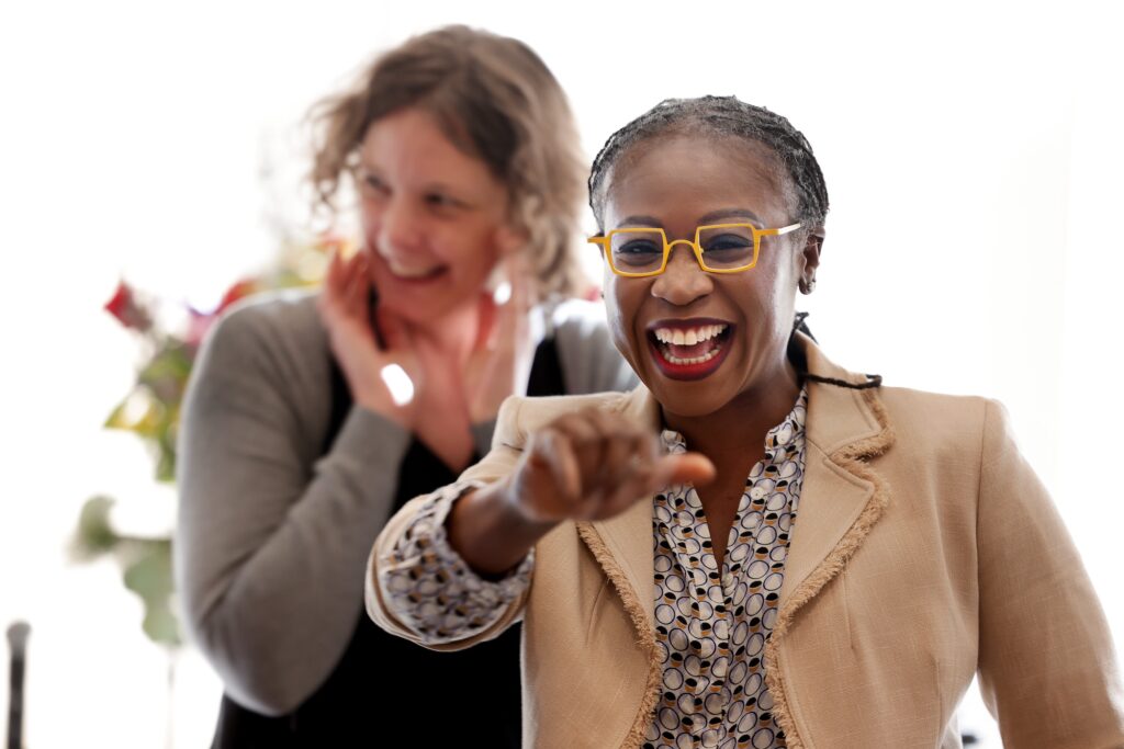 Eniola-Adefeso smiles broadly in the foreground, looking at someone just past the camera, while Stevens, in the background, smiles at someone out of the frame.
