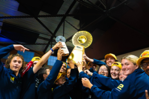College students smile while holding up a gold trophy