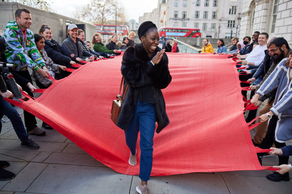 A photo of a woman smiling after walking off a carpet held aloft by multiple people