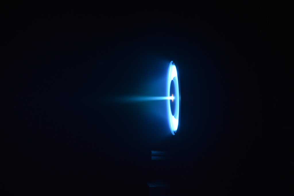 The thruster glows as a pale blue ring with a disk-shaped shadow in middle, and a blue ray streaking out from the center.