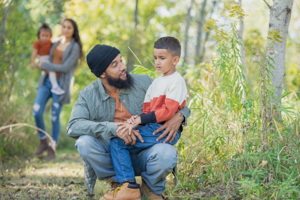 A young boy sits on his father's lap as his dad bends down during a family walk to take a break with his son.
Image credit: FatCamera, iStock
