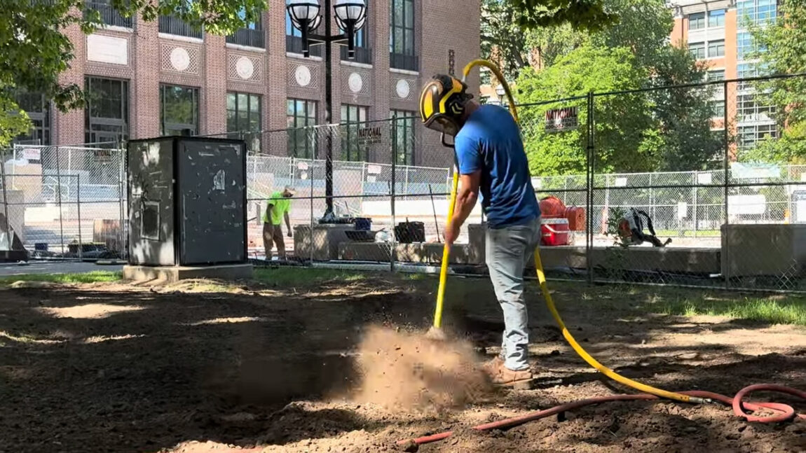A construction worker uses a tool to blast sand and dirt
