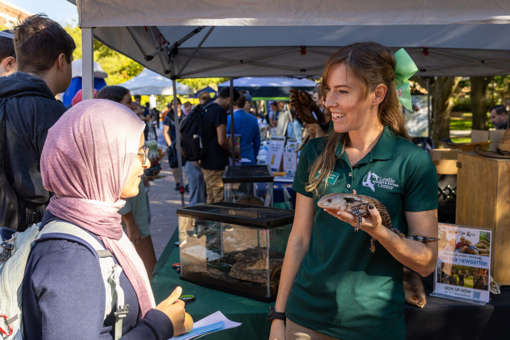 A woman holding an iguana speaks to another woman at an outdoor event