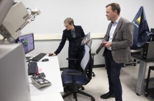 In a research lab, a woman stands in front of a computer and navigates while a man in a suit watches the demonstration.