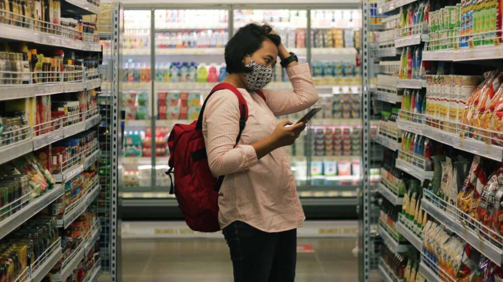 A woman holds her hand to her head looking at her phone in the grocery store. Image credit: Viki Mohamad, Unsplash