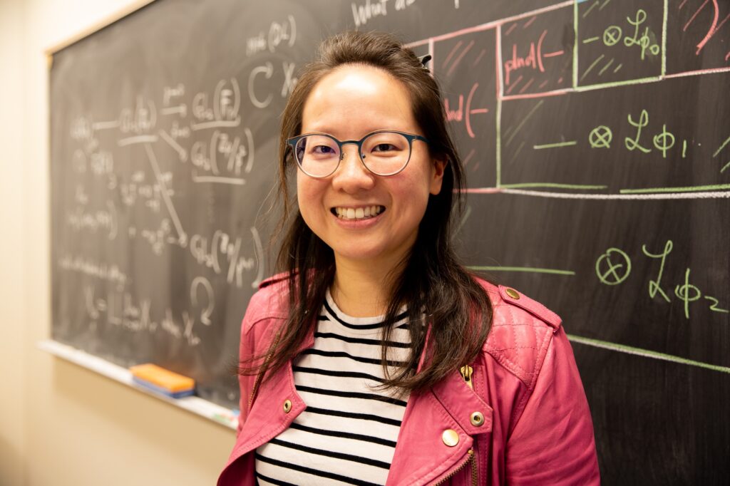 Charlotte Chan stands in front of a chalk board with equations written on it in white, green and pink chalk.
