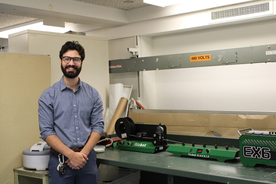 A man stands with his arms folded in front of him and smiles