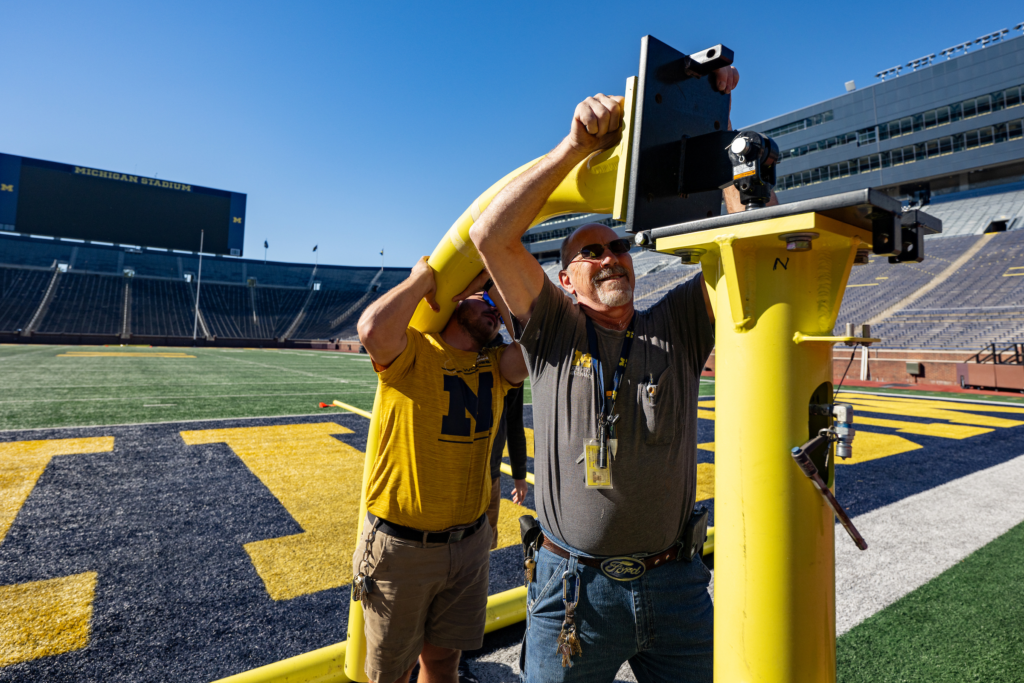 Several people hold up a yellow goal post while one person attempts to install it