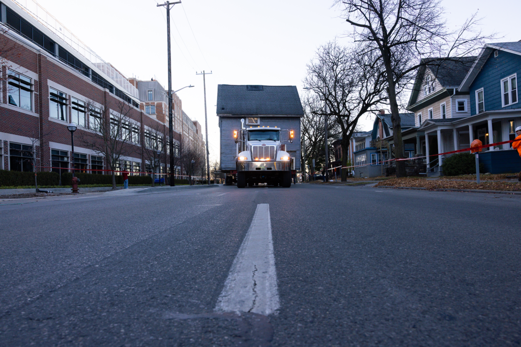 A house is hauled down a street by a trailer and truck