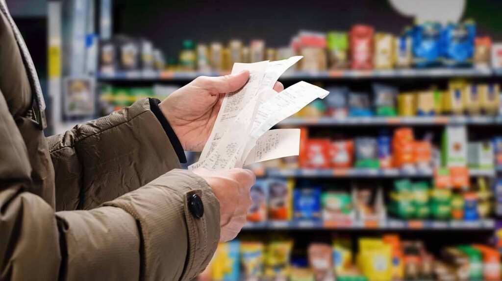 A man viewing receipts in supermarket and tracking prices. Image credit: Adobe Stock