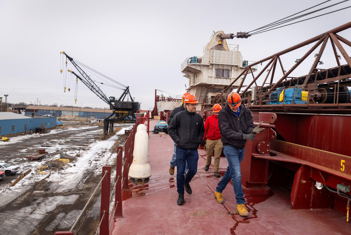 Four engineers walk down the red deck of a large freighter.