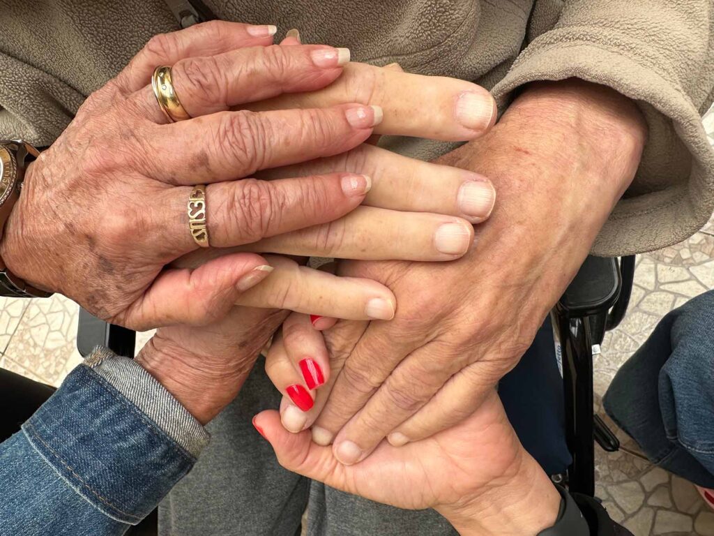 Four hands of different ages rest gently on top of one another, showing generational care and connection. Image credit: Fernanda Pires