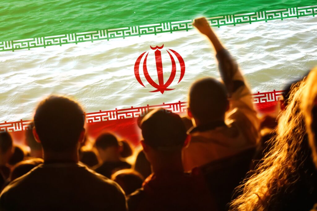 A crowd protesting in front of the Iranian flag. Image credit: Adobe Stock