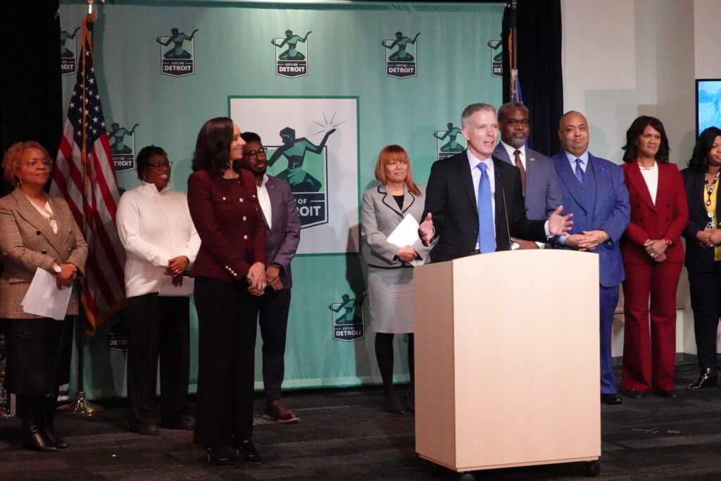 Luke Shaefer speaks at the podium while Detroit Mayor Mary Sheffield, left, looks on. Image courtesy: Poverty Solutions