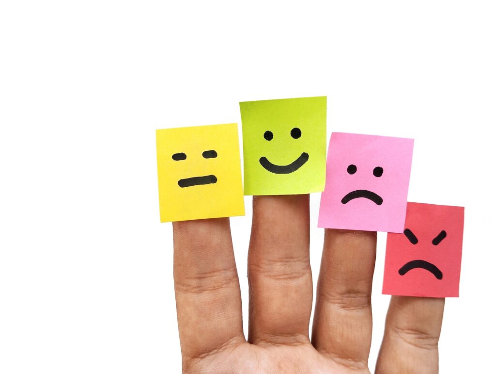 Happy, neutral, sad and angry emoji on colorful sticky note paper attached to the finger, conceptualizing mental health. Image credit: Adobe Stock