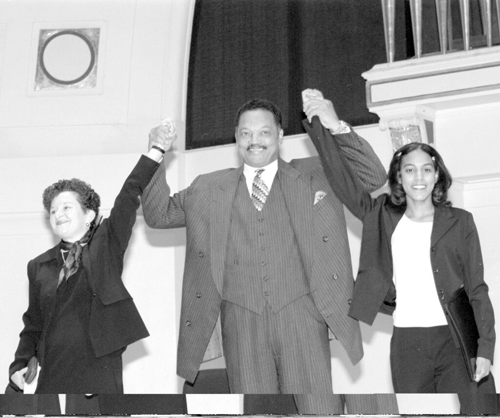 A man in between two women raise their arms in the air while smiling