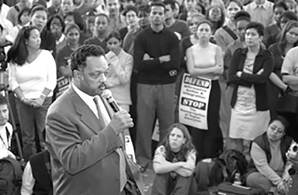 A man with a microphone speaks to a crowd of people gathered near him