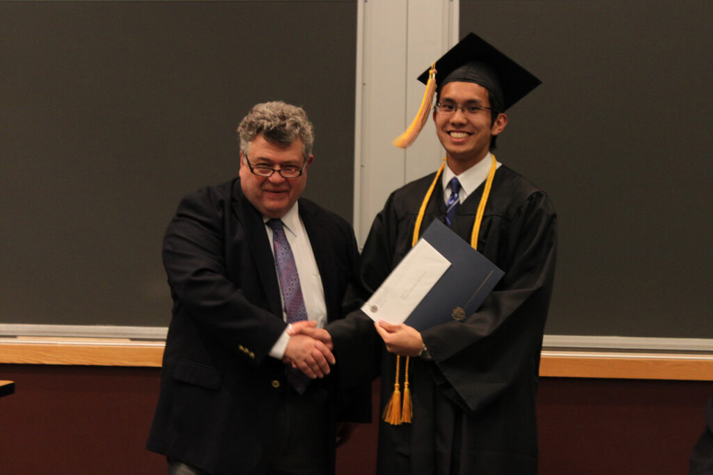 A man shakes the hand of another man who is wearing a graduation cap and gown