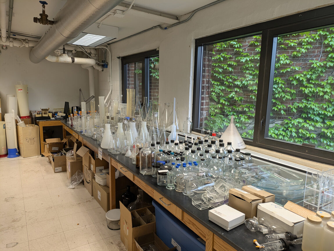 Lab materials like test tubes and glass bottles are lined up on a lab table
