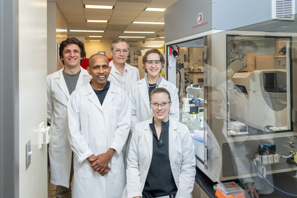 Five people in white lab coats pose for a picture smiling