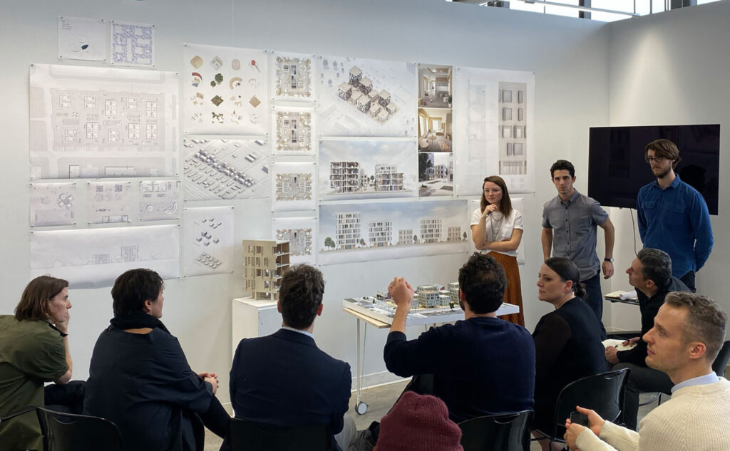 People sit and stand around drawings of buildings