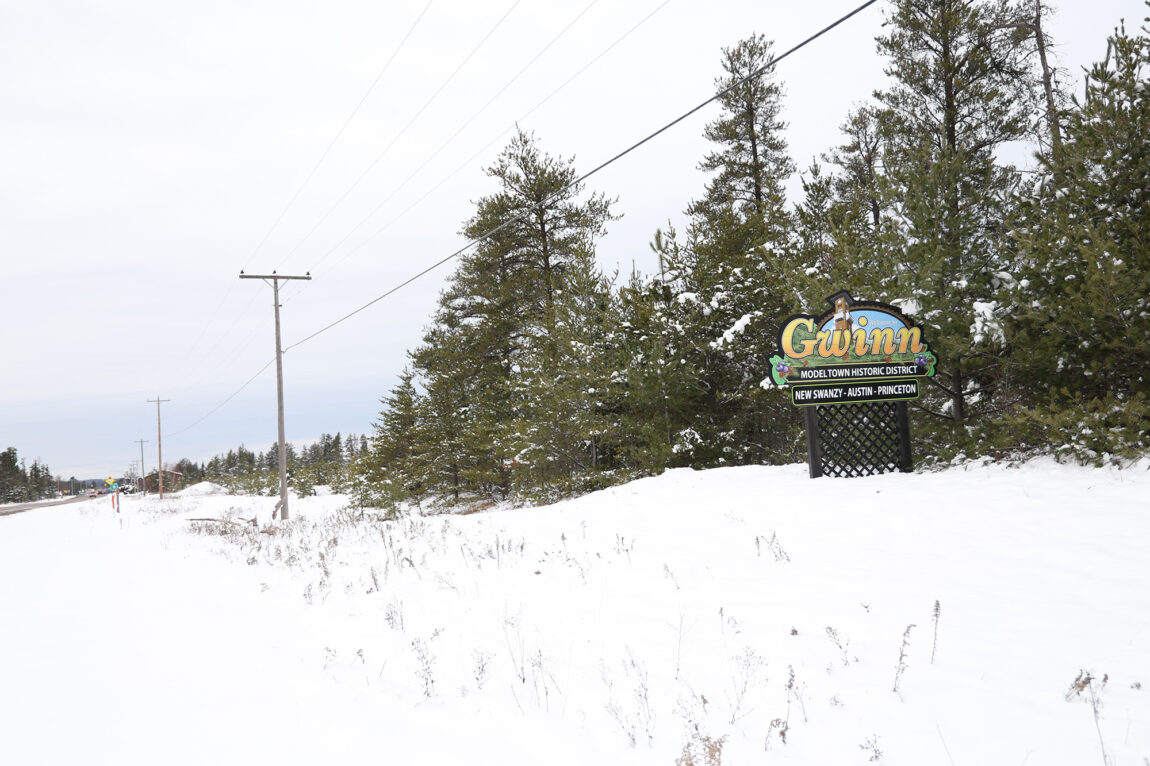 A sign that says "Gwinn" sits off a snowy roadway