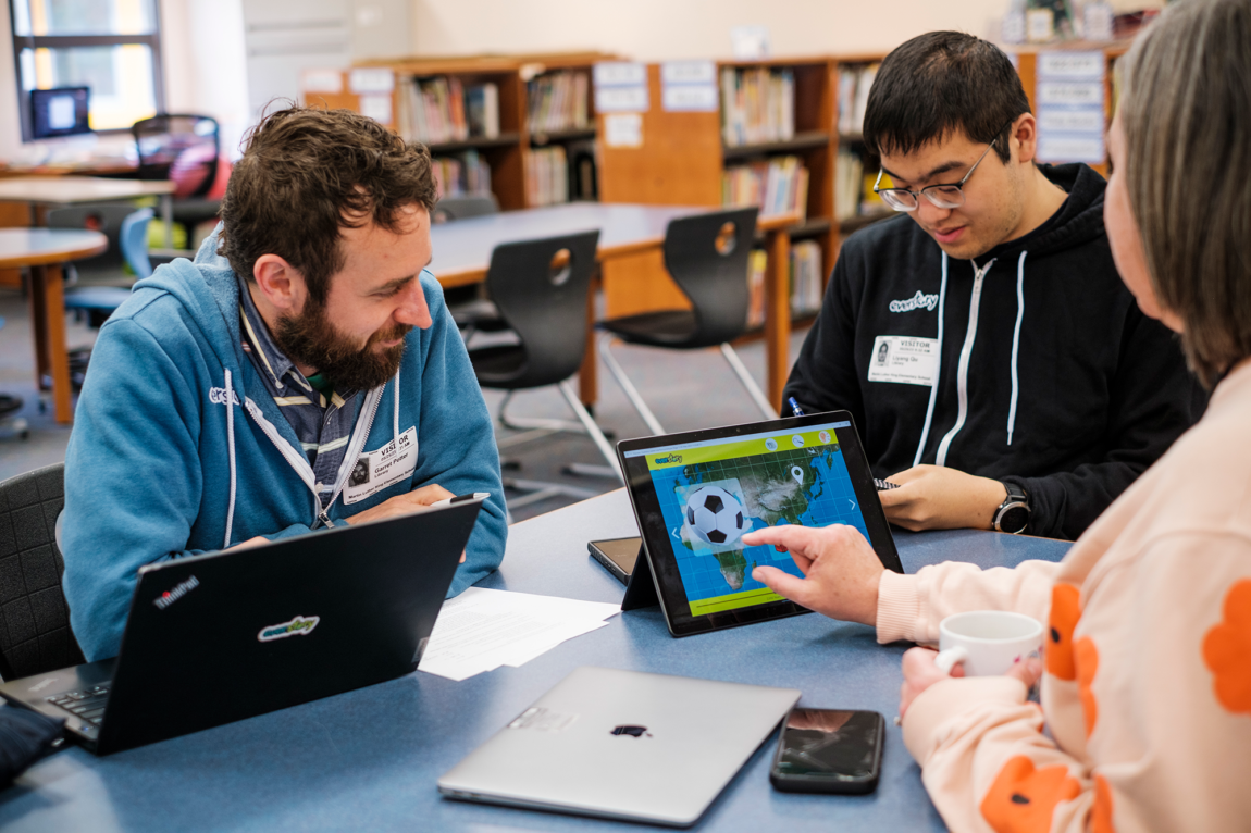 Three people at a table with a laptop and a tablet
