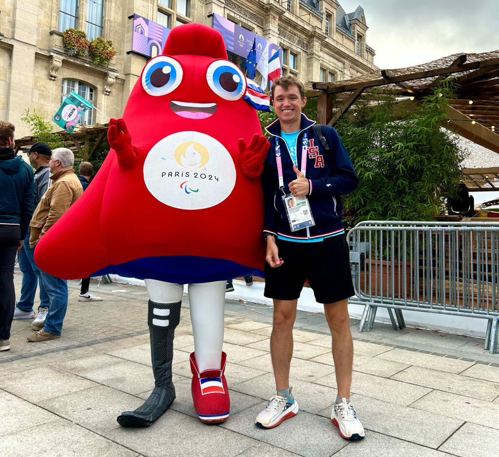A man stands next to a red mascot