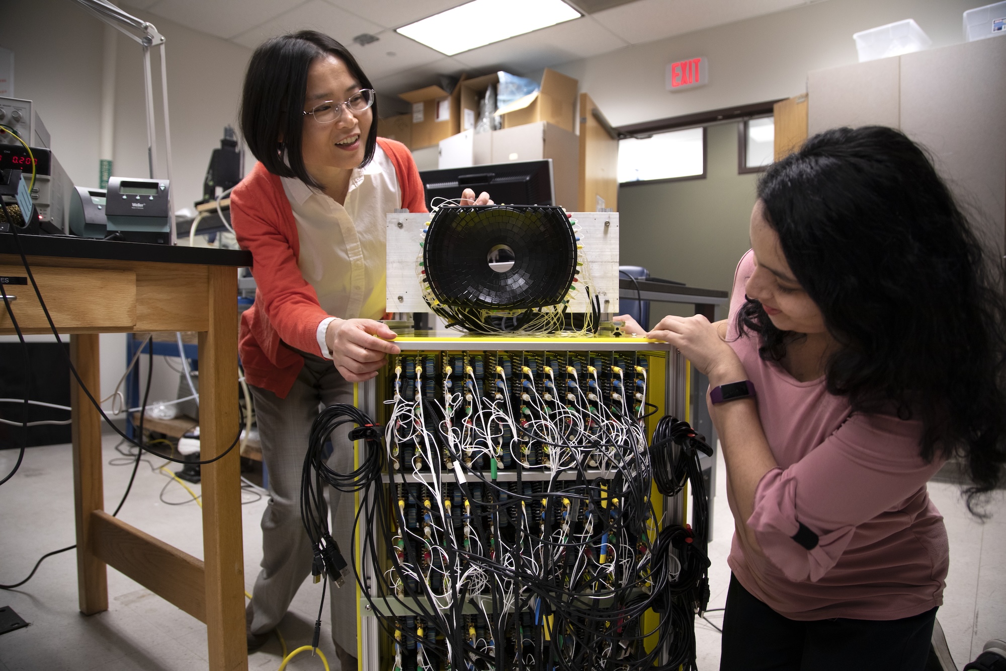 Two researchers adjust a complex-looking device with many rows and columns of wires.