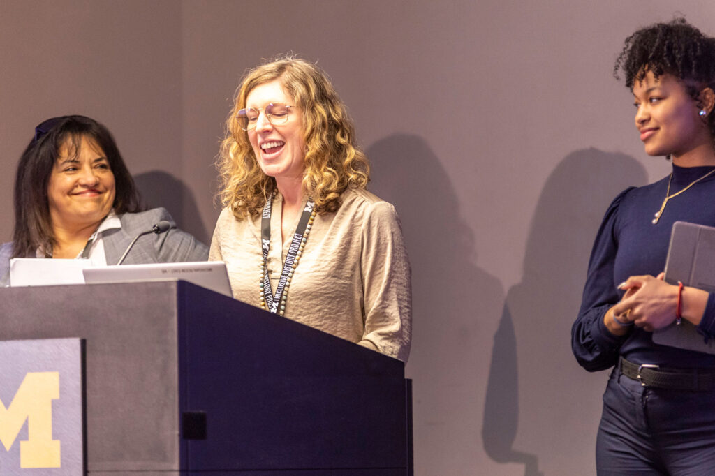 Three women stand at a lectern with one of them speaking