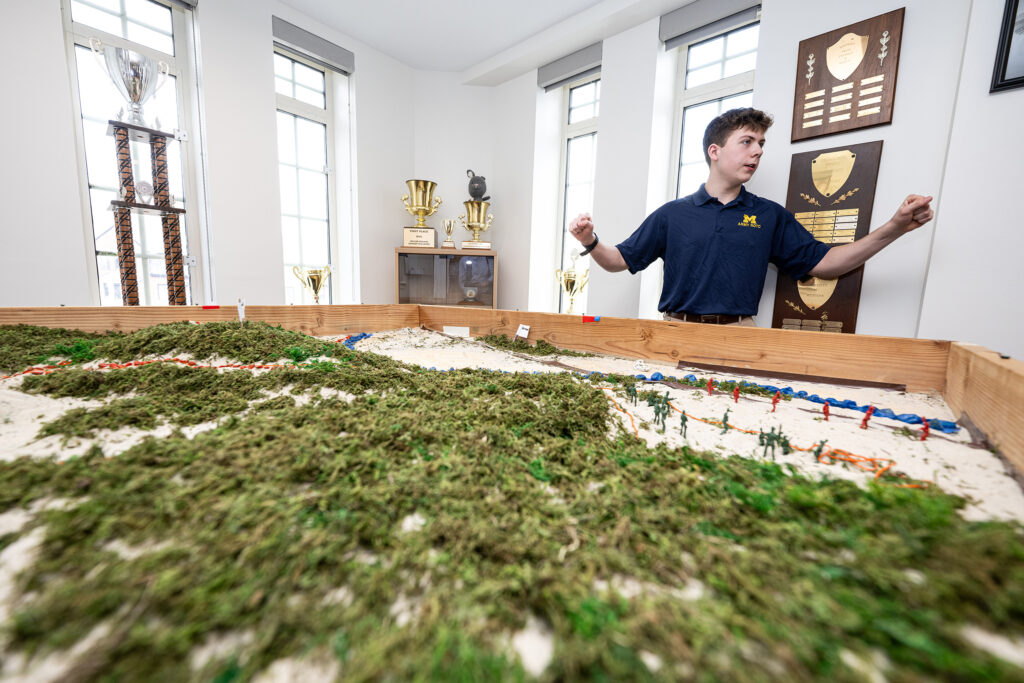 n Army cadet stands beside a model of Nichols Arboretum, where cadets use miniature soldiers to plan tactical operations

