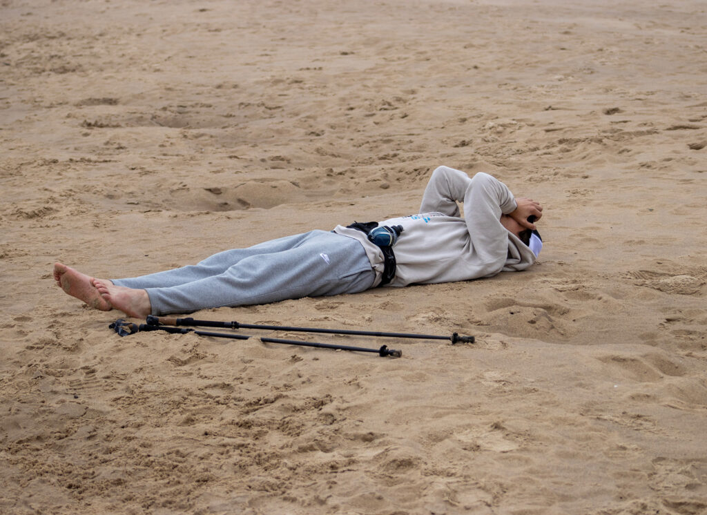 A man lays on a beach wearing great sweatpants and a gray sweatshirt