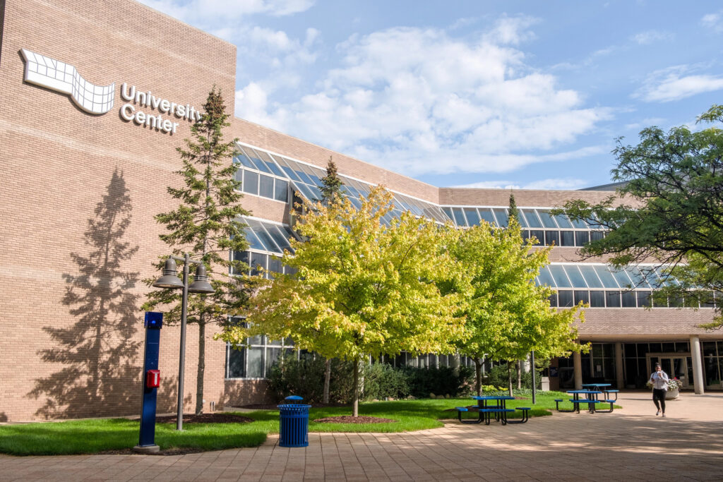 A brick building with several trees in front and a stoned walkway in the foreground