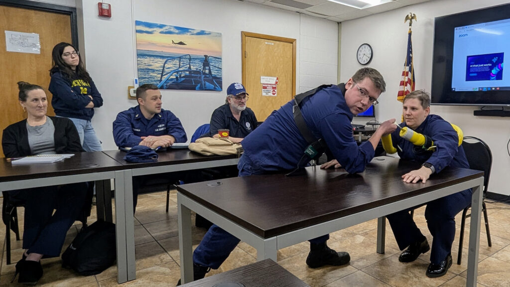 Four people watch as a man and a woman use a device to simulate a water rescue