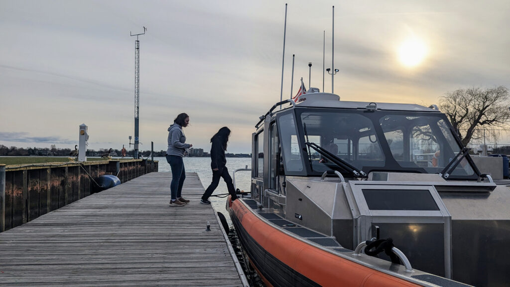 Two people prepare to step aboard a small vessel while it sits at a dock