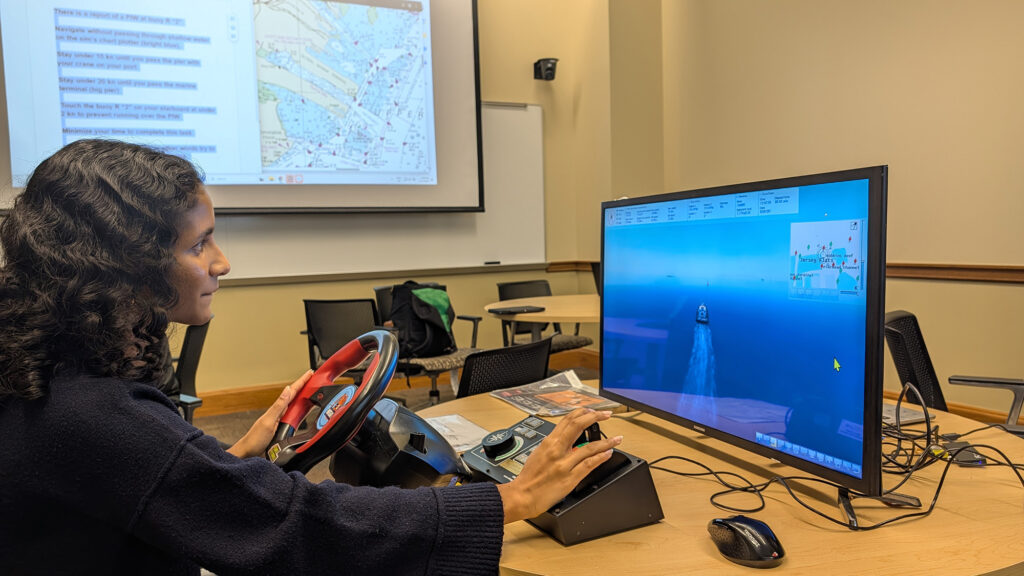 A woman uses a steering wheel attached to a computer to simulate driving a rescue boat