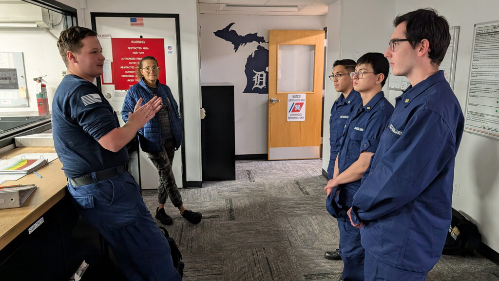 Two Coast Guard personnel speak to three students while standing in a building
