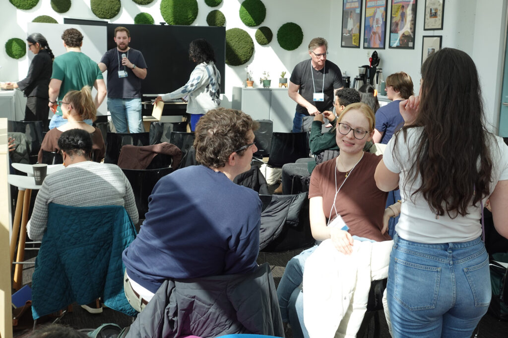 Several people in a room sitting and standing and talking to each other